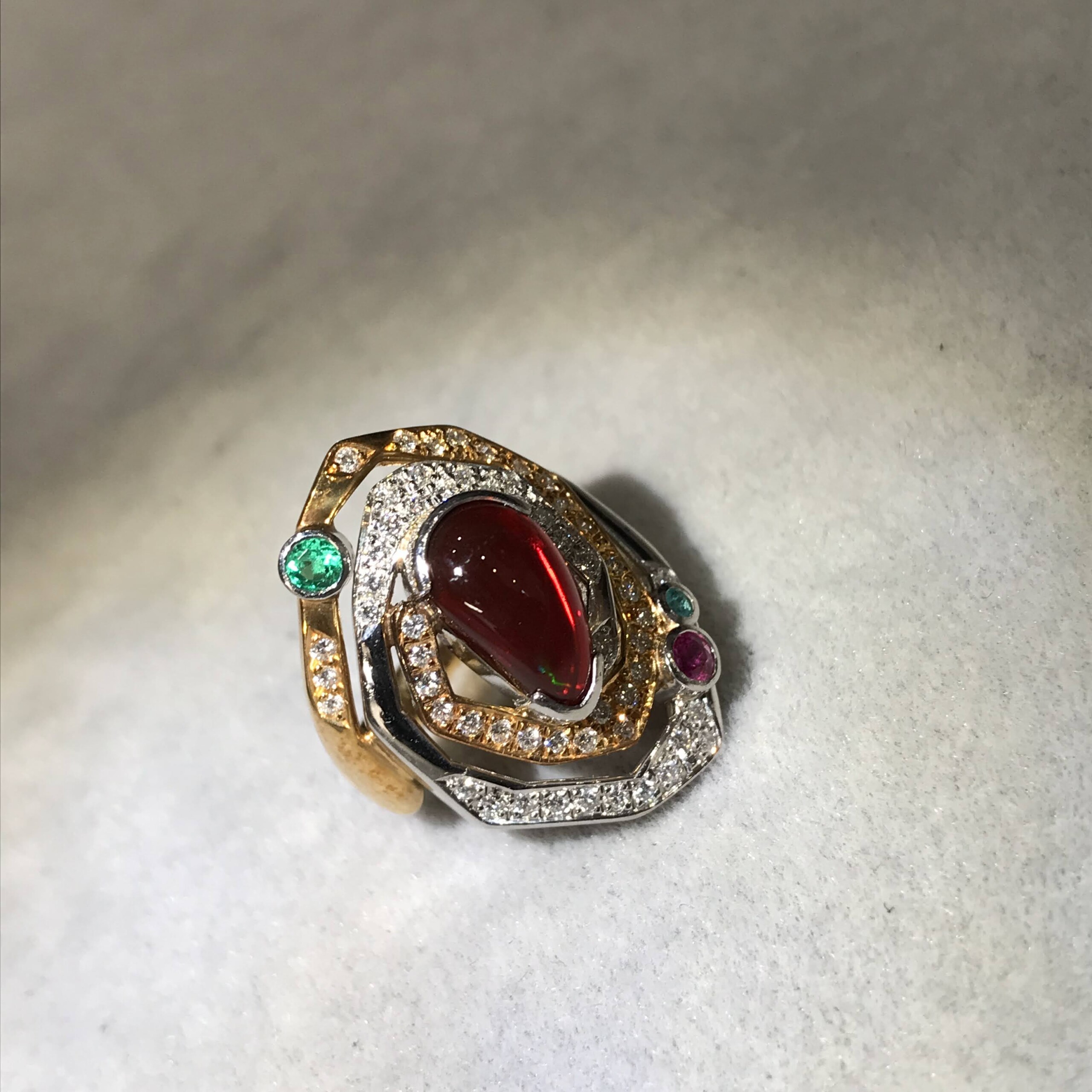 A ring with 18K gold and platinum setting, abundantly featuring garnet, emerald, aquamarine, and diamonds.